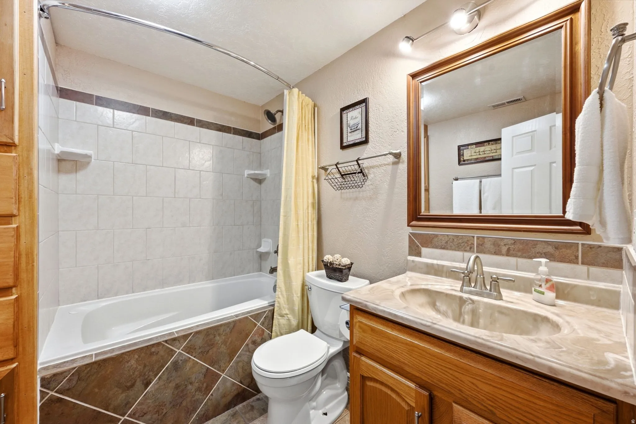Built-in bathtub with subway tile surround, vanity with an integrated sink, wood-finish cabinetry, and a framed wall mirror