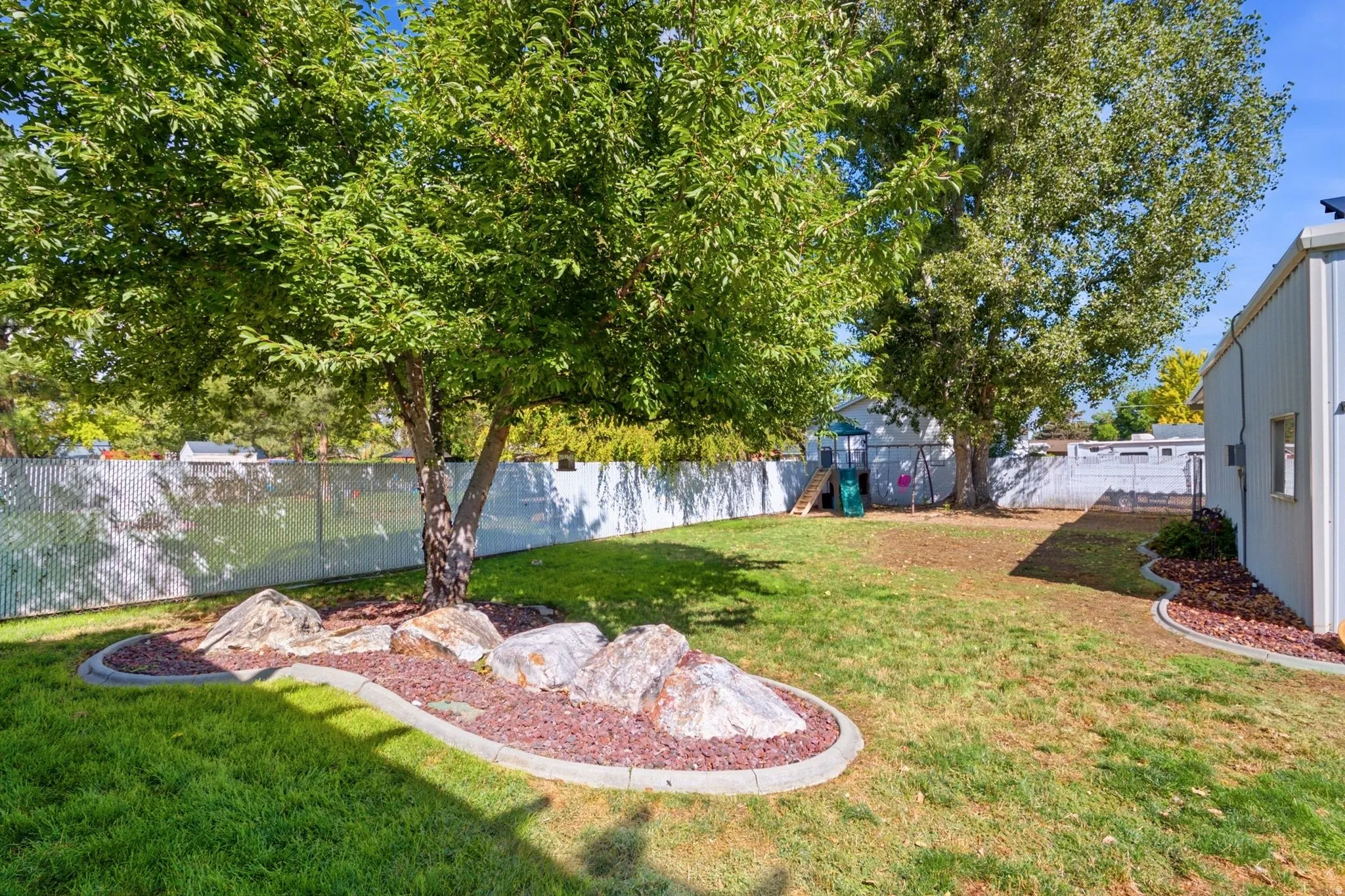 Expansive grass lawn with mature trees and decorative rock landscaping