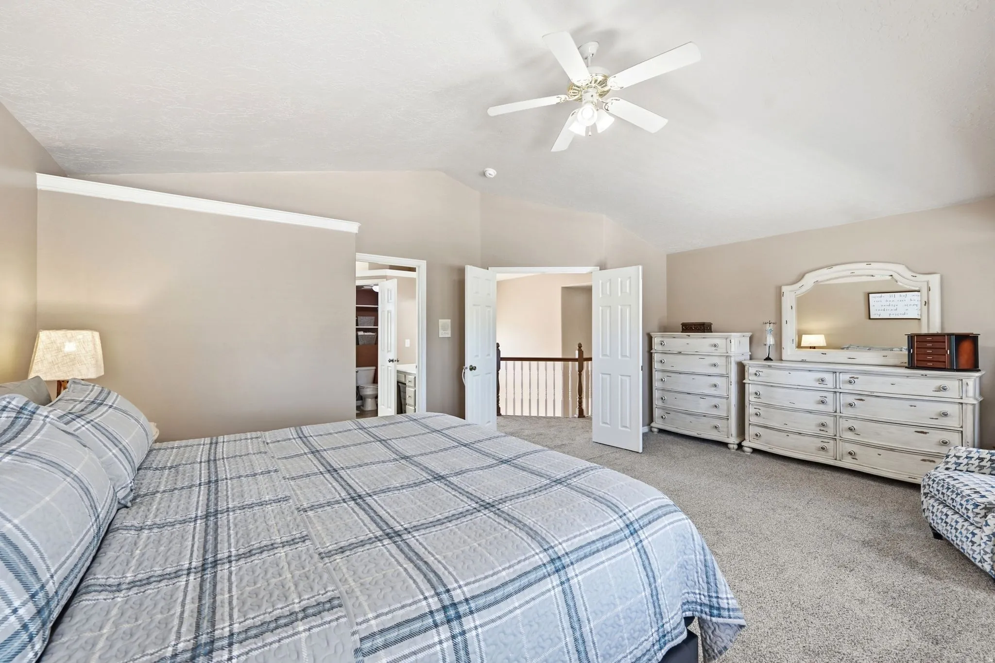 Vaulted ceiling with a ceiling fan, carpeted flooring, and a doorway opening to a bathroom