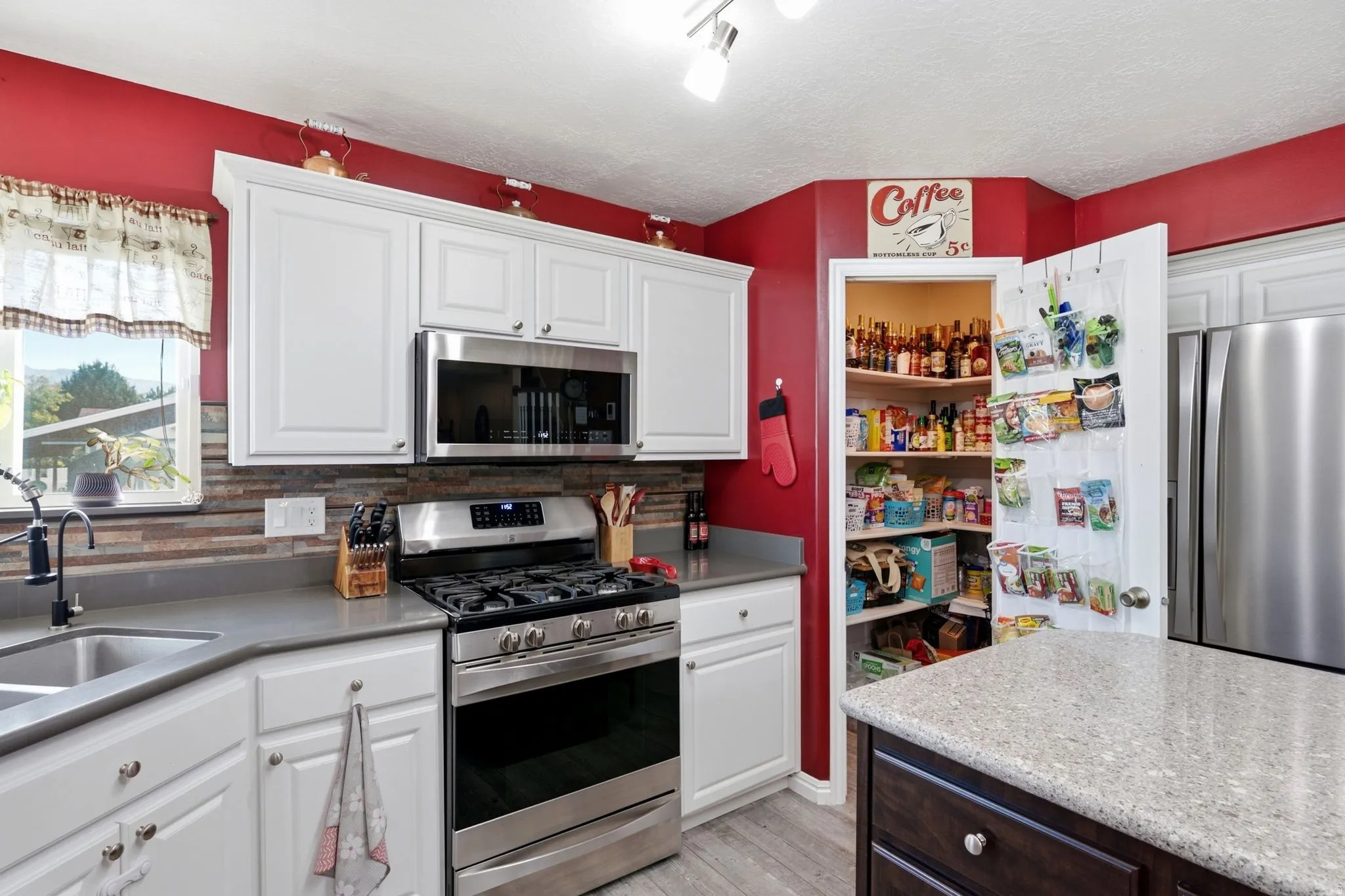 White cabinetry with stainless steel appliances, stone slab countertops, and a full pantry