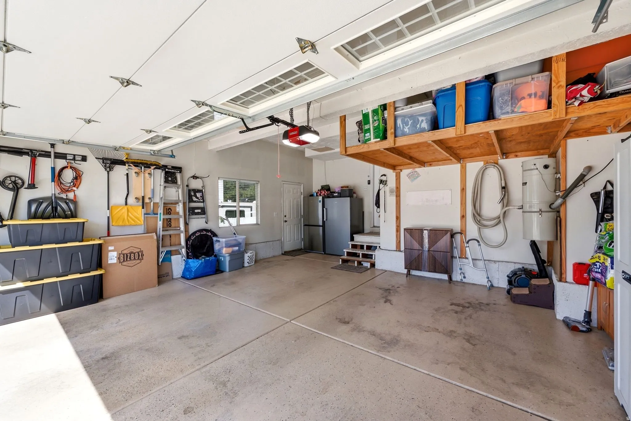 Attached garage with a concrete floor, overhead storage shelving, and a side access door