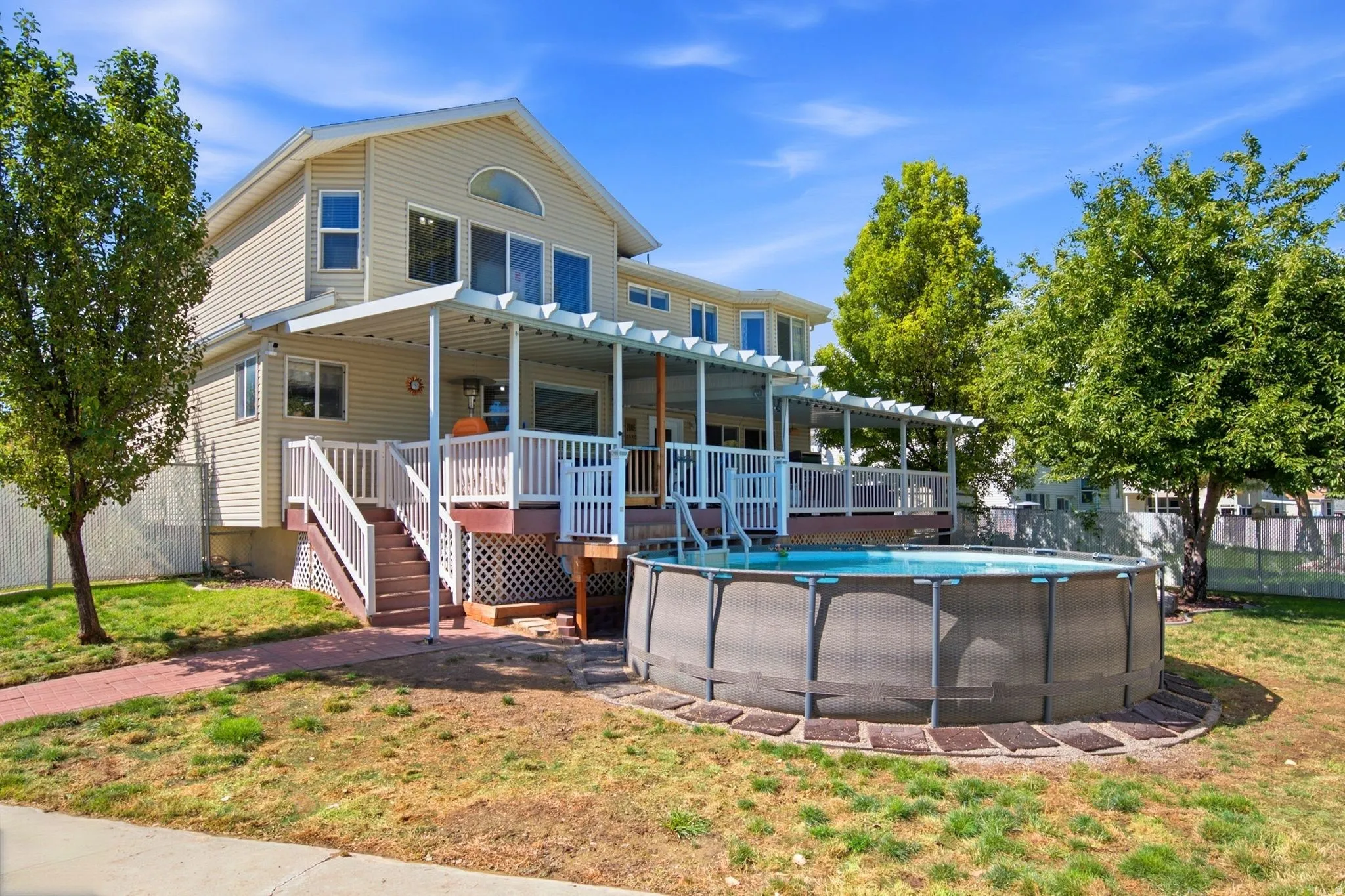Rear exterior featuring vinyl siding, an extensive elevated deck with white railings and pergola, an above-ground swimming pool, and mature trees