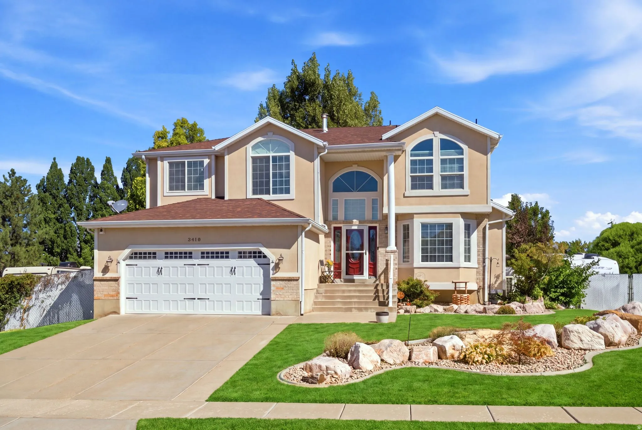 Stucco exterior featuring multiple arched windows, an attached two-car garage, a concrete driveway, and a landscaped front yard with decorative rocks