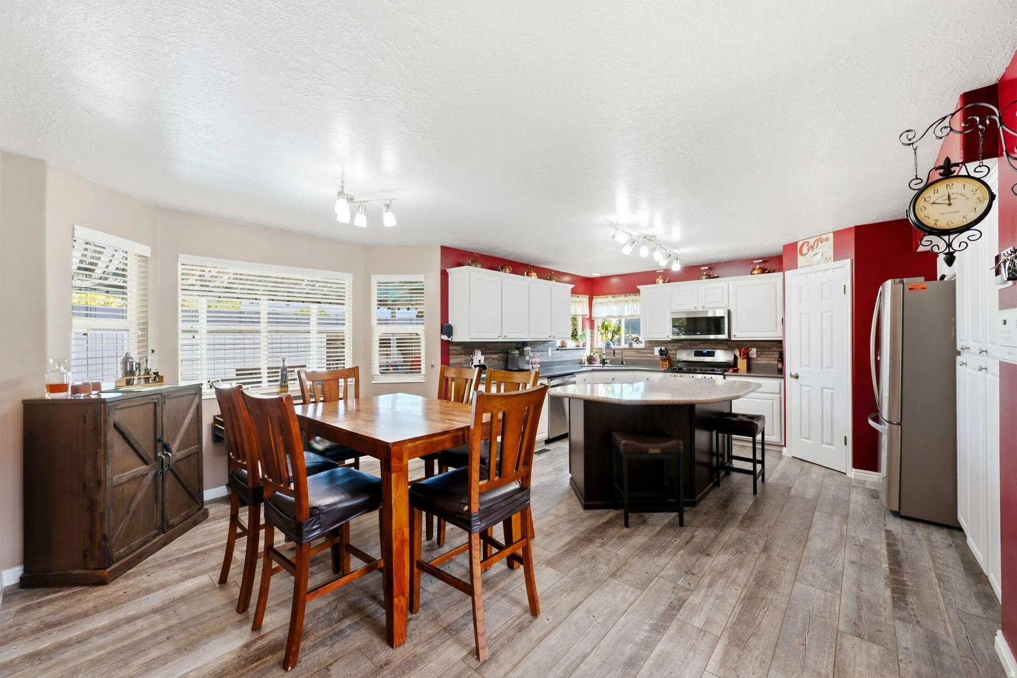 Open-concept layout featuring white cabinetry, stainless steel appliances, a kitchen island with seating, and wood-finish flooring