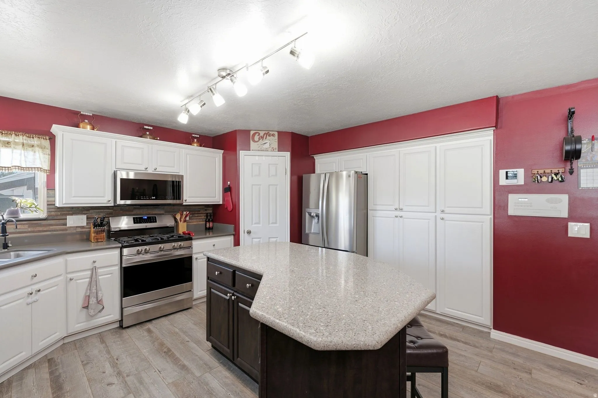 White cabinetry with stainless steel appliances, a center island with a stone-finish countertop, and wood-finish flooring