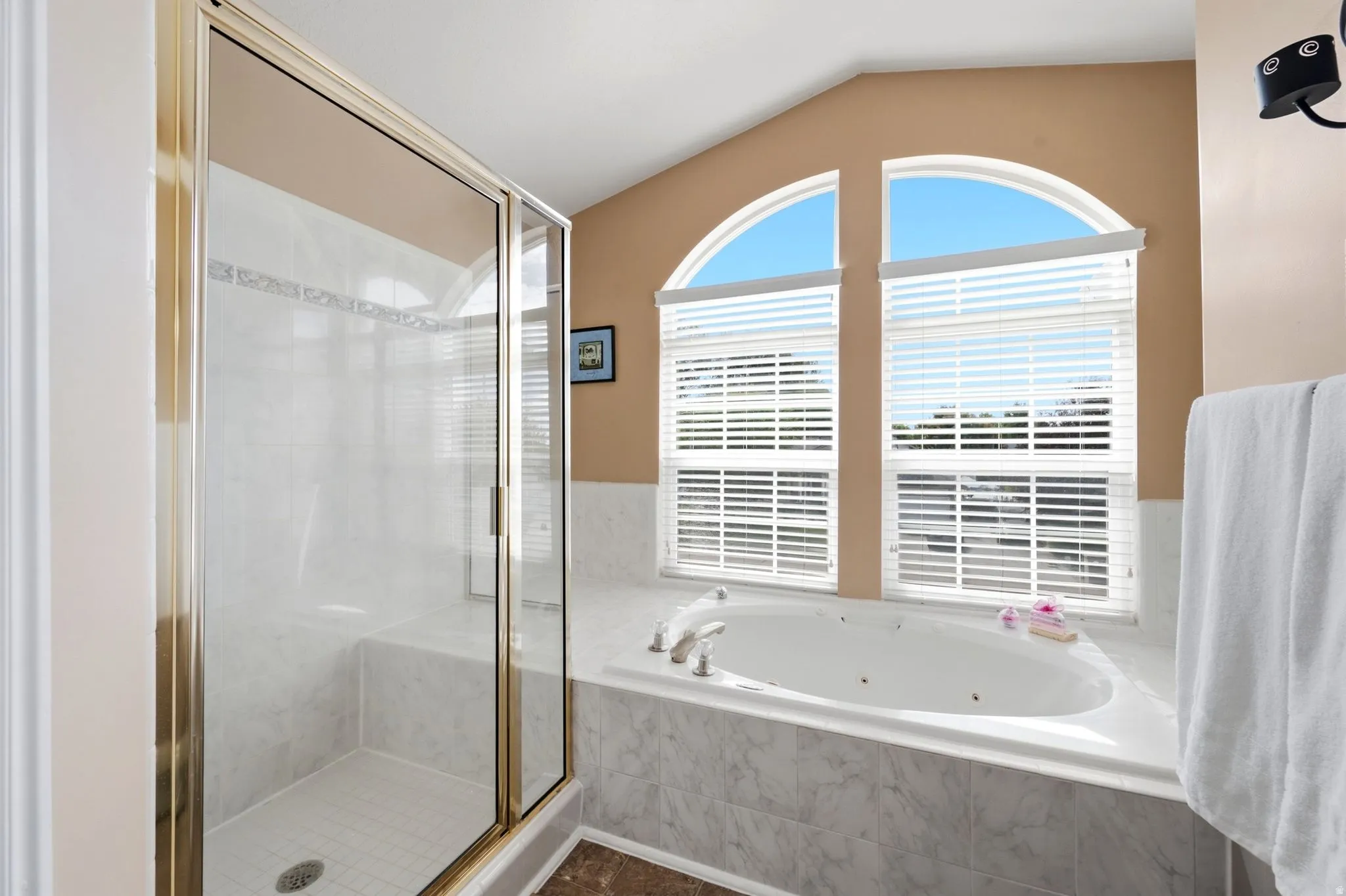 Glass-enclosed shower with a built-in bench, jetted soaking tub, and arched windows with horizontal blinds