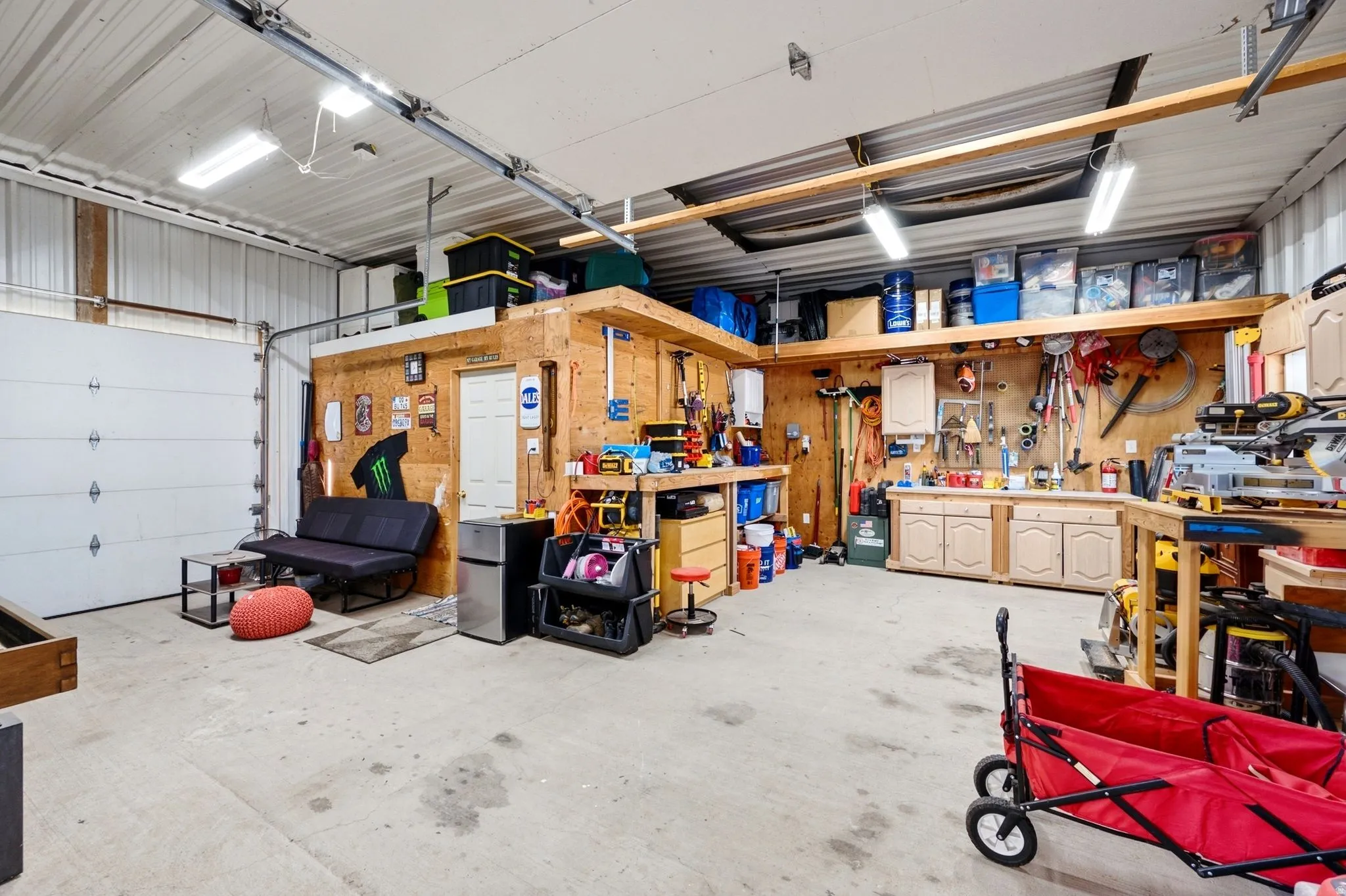 Spacious garage with exposed metal siding, concrete flooring, overhead fluorescent lighting, and built-in wood shelving and cabinetry