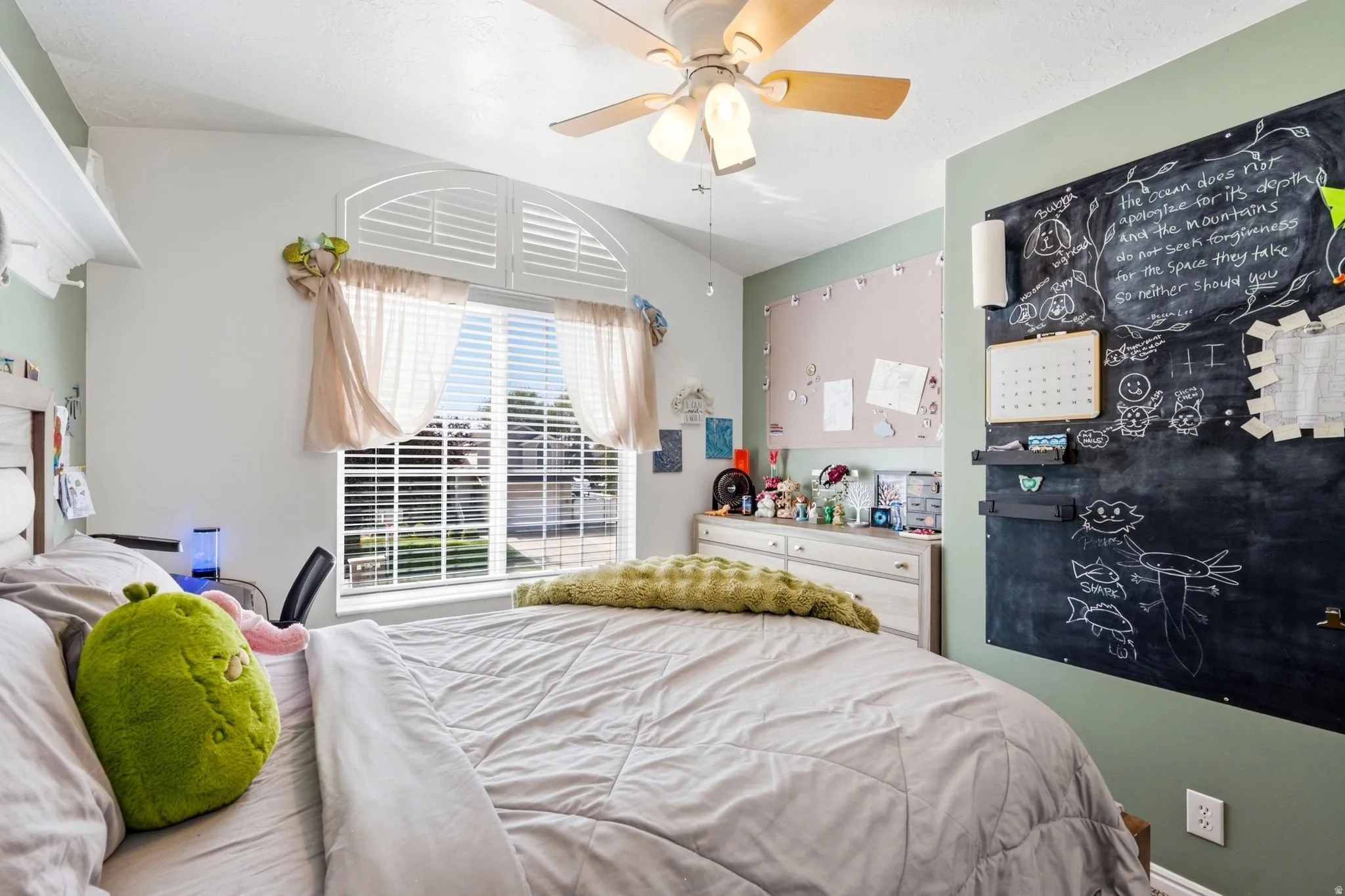 Vaulted ceiling with a ceiling fan, arched window with plantation shutters, custom built-in shelving, and a decorative accent wall