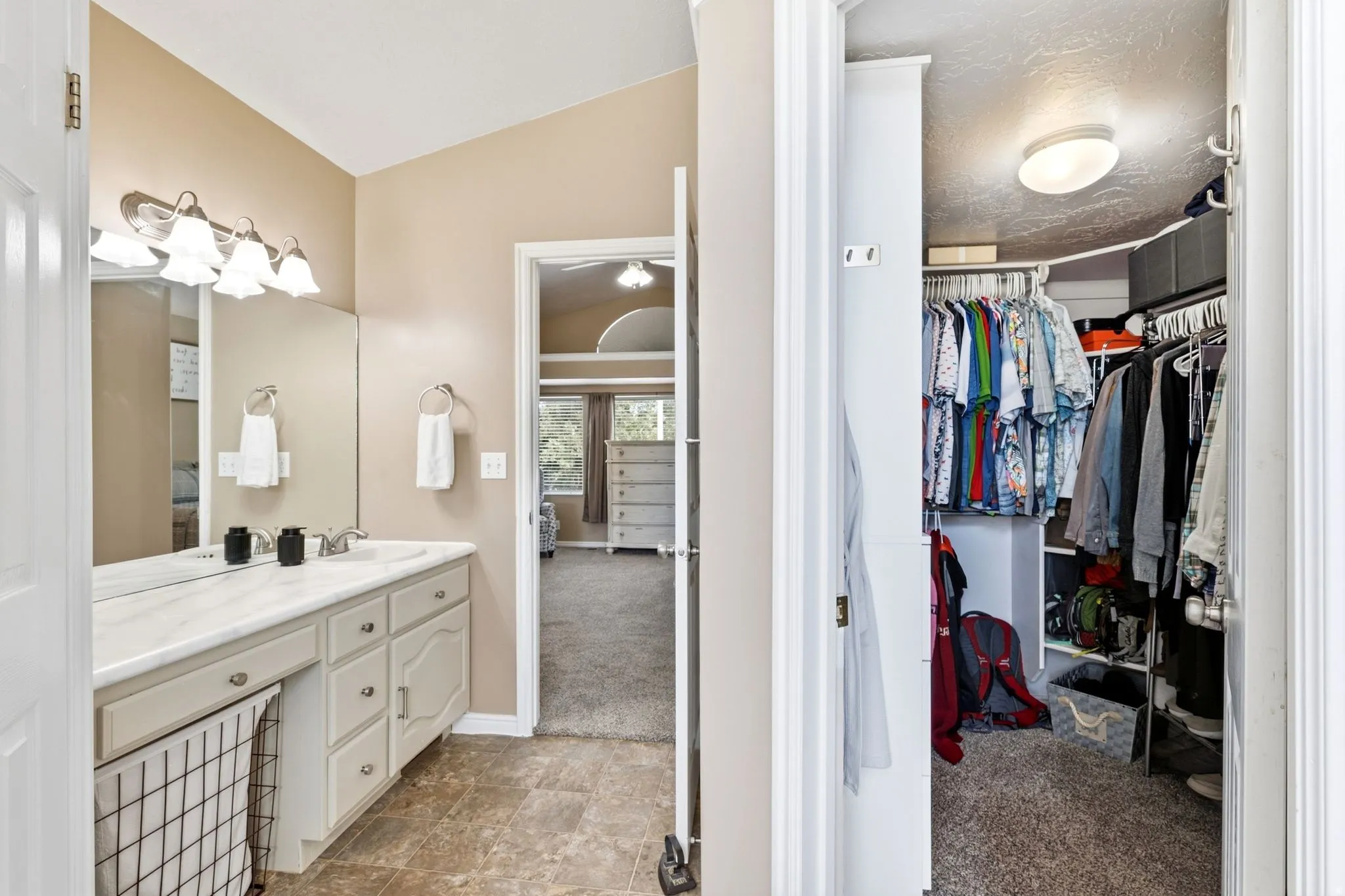 Vanity with an integrated sink and base cabinetry, wall-mounted light fixture, and a built-in closet with shelving and hanging rods
