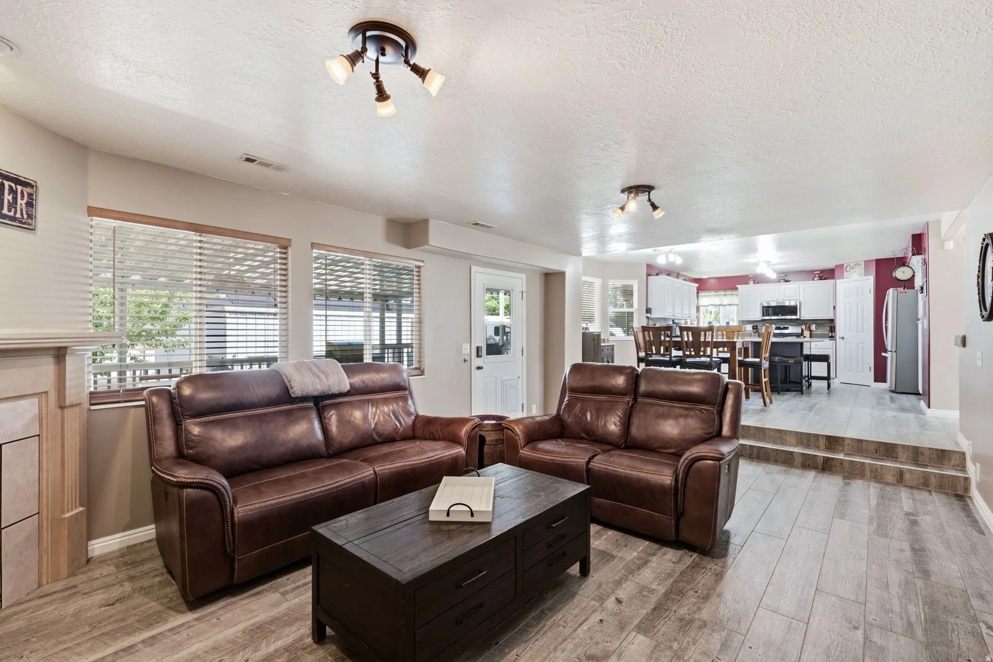 Living area featuring wood-finish flooring, a white trim fireplace surround, and multiple windows with blinds