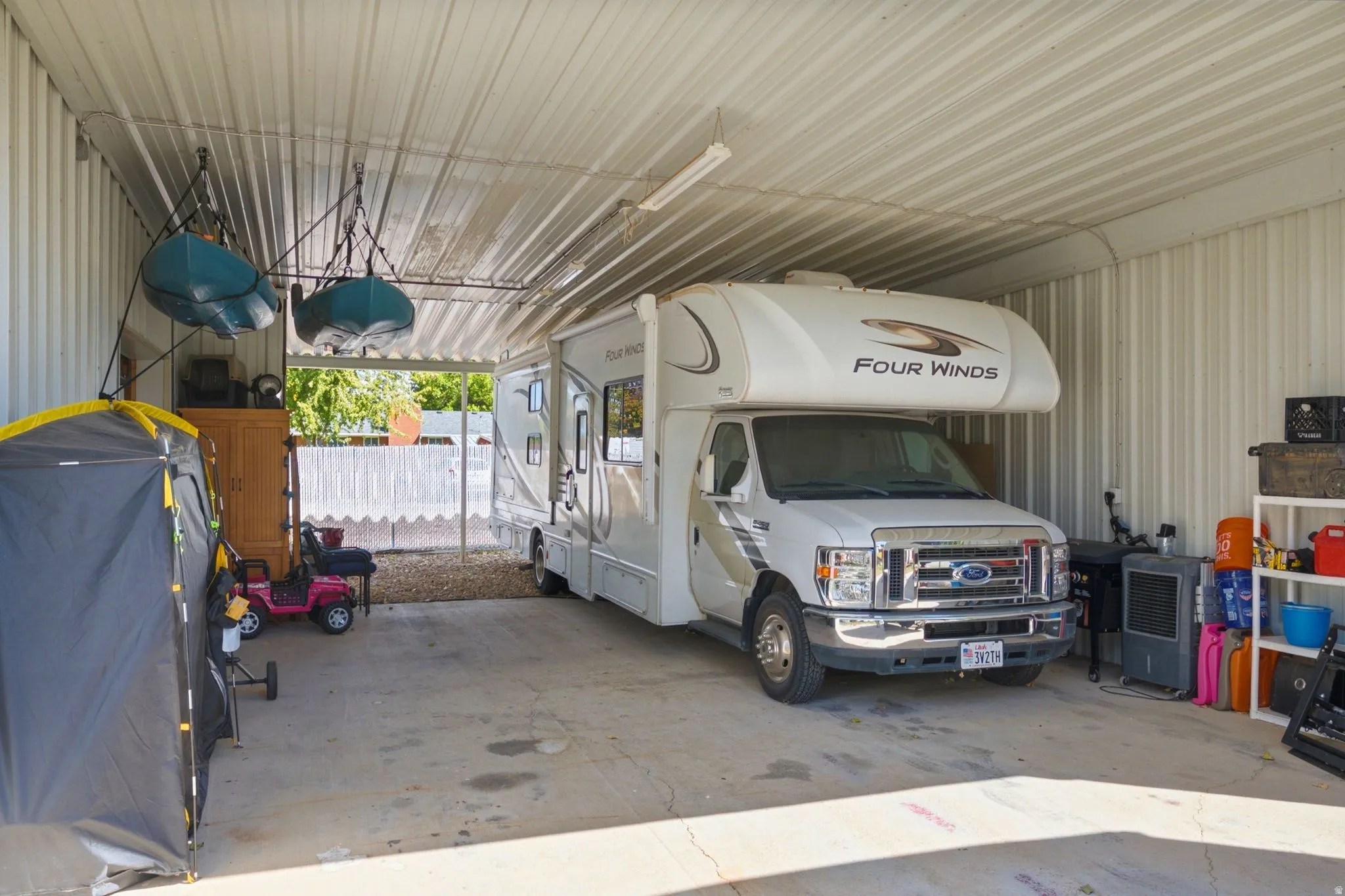 Enclosed metal carport with a corrugated metal roof, concrete flooring, and an open side for access