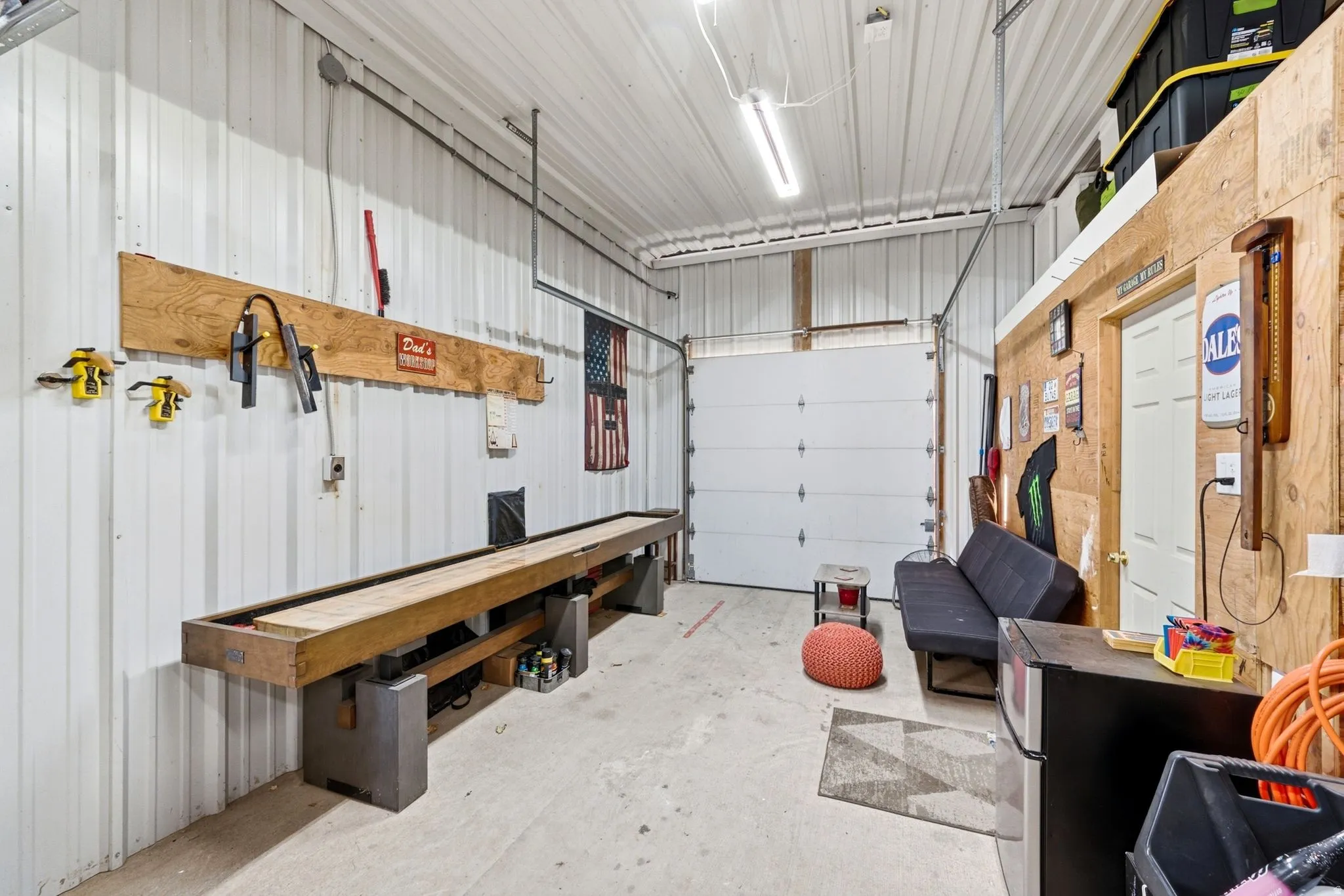 Metal corrugated walls, concrete flooring, overhead fluorescent lighting, and a white paneled garage door