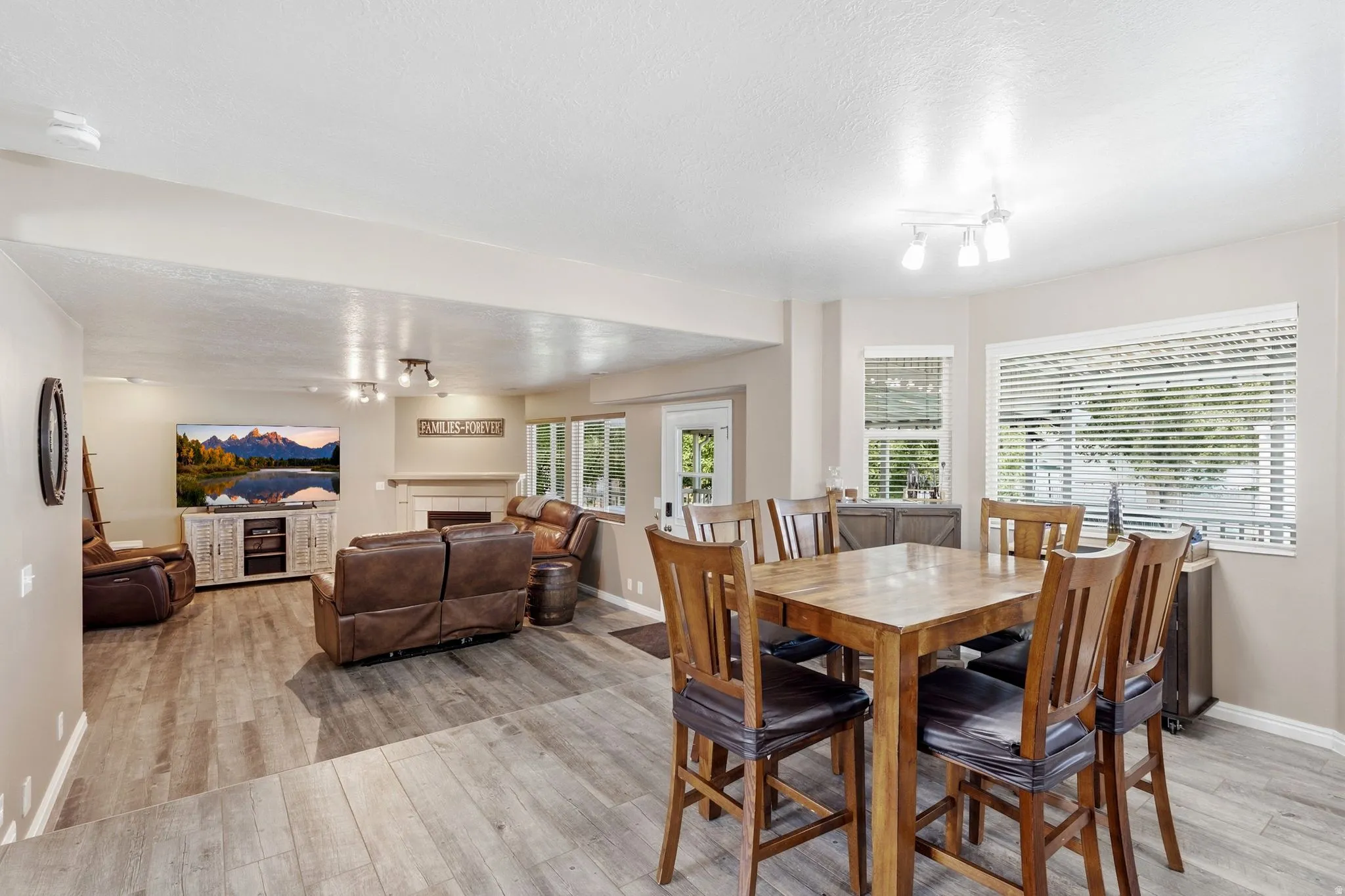 Open-concept living and dining areas featuring wood-finish flooring, recessed lighting, a built-in fireplace with a mantel, and multiple windows