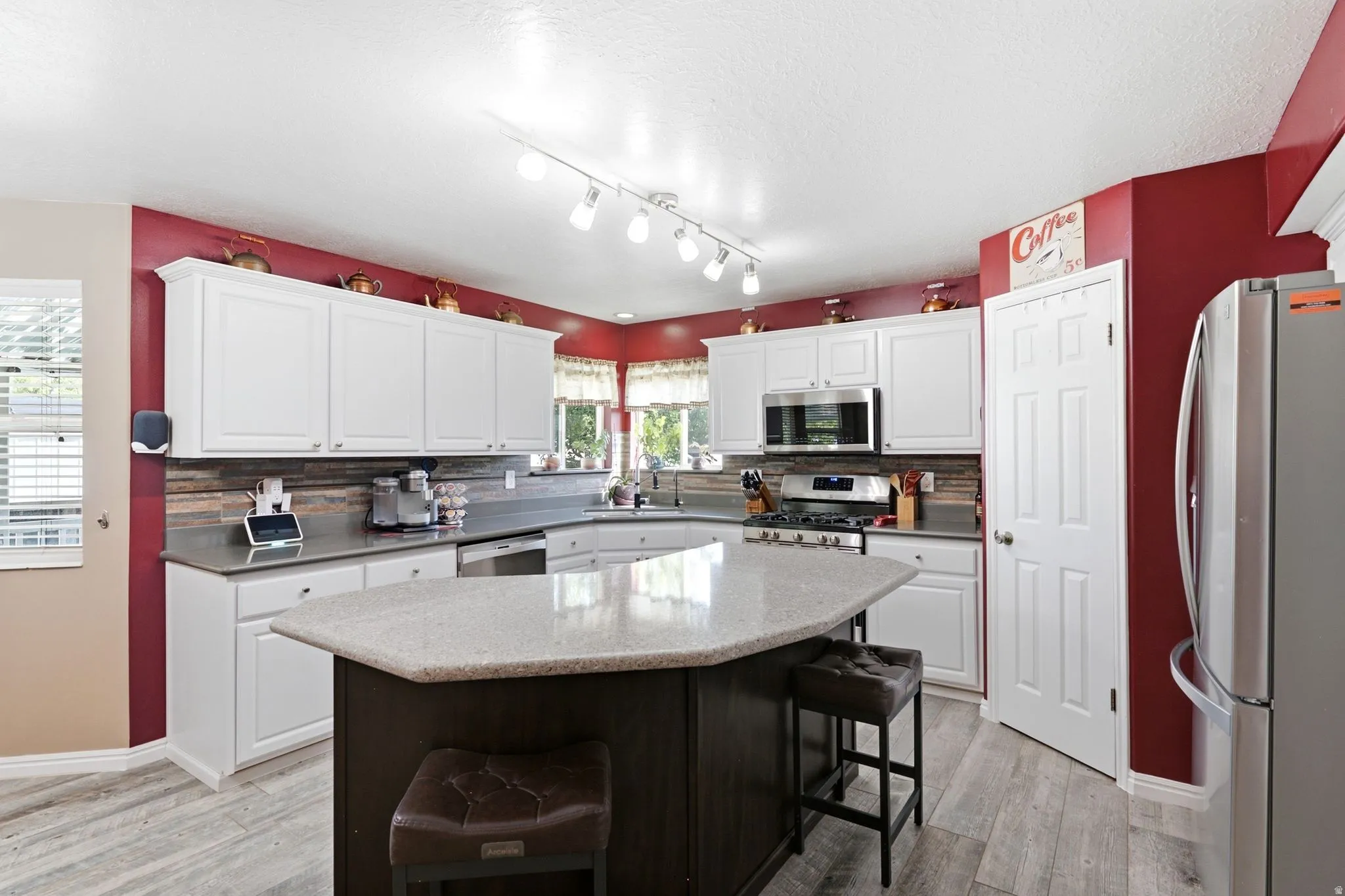 Kitchen featuring white cabinetry, stainless steel appliances, a multi-tone tile backsplash, a center island with countertop seating, and wood-finish flooring