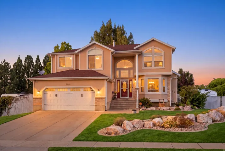 Stucco exterior with a two-car garage, concrete driveway, and professional landscaping featuring rock accents