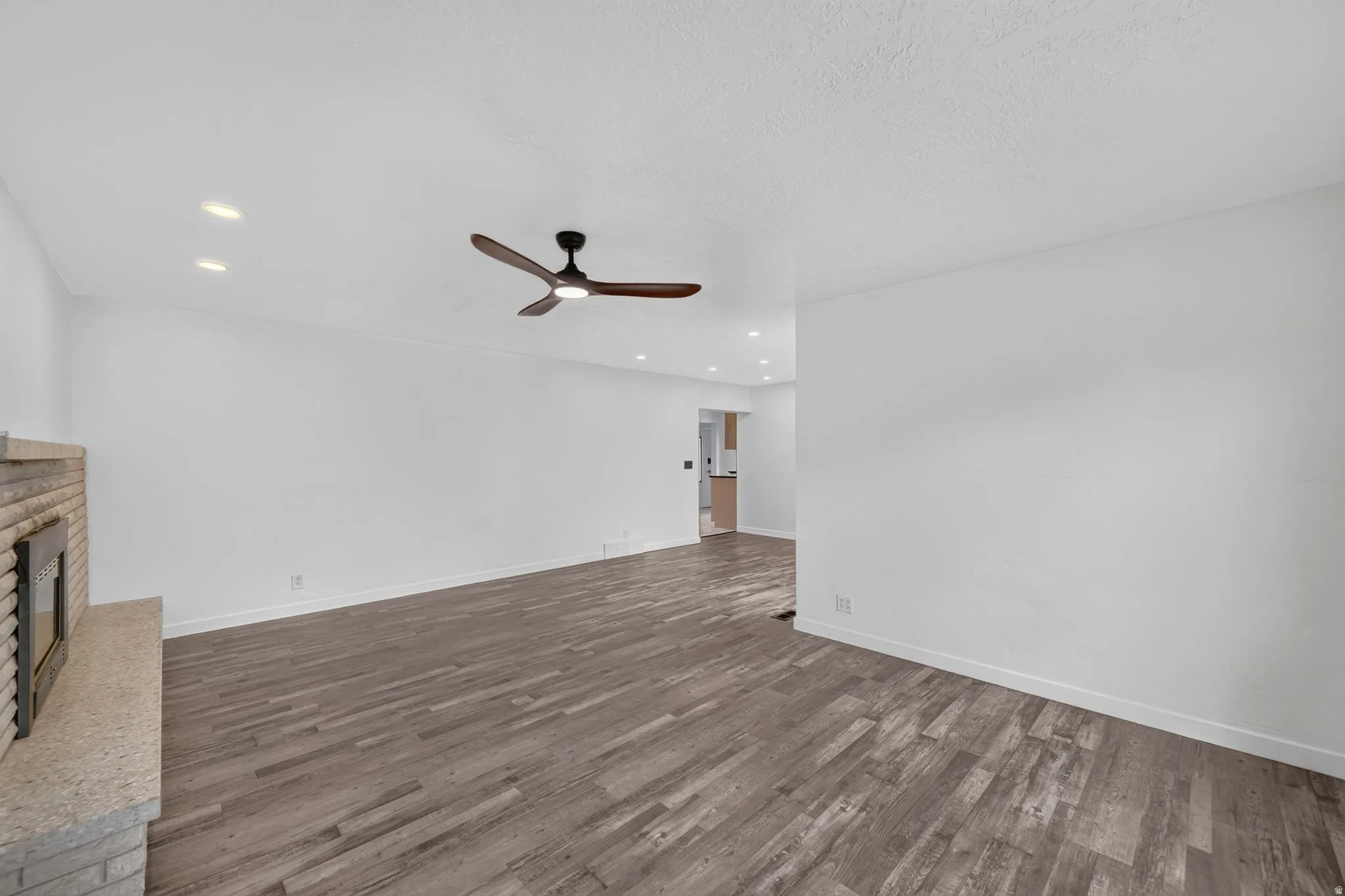 Spacious living area featuring wood-finish flooring, a stone fireplace, recessed lighting, and a ceiling fan