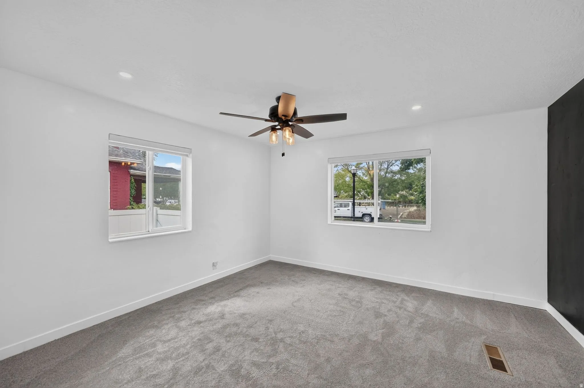 Spacious bedroom room with plush gray carpeting, recessed lighting, and a ceiling fan.