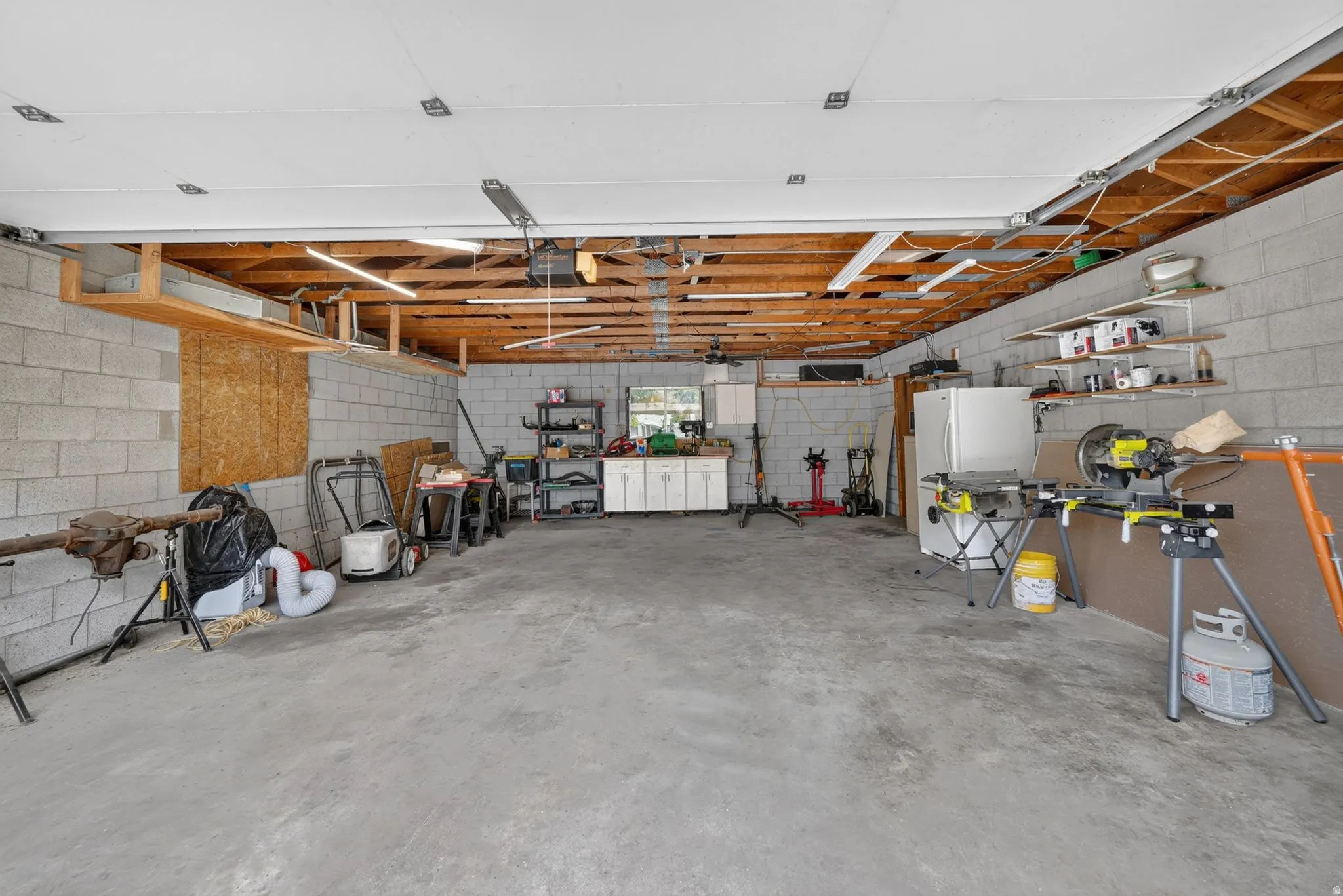 Spacious garage featuring concrete block walls, exposed wood beam ceiling, concrete flooring, and built-in shelving