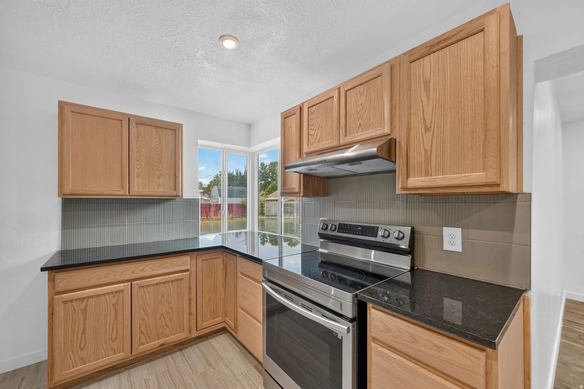 Kitchen featuring wood-finish cabinetry, dark countertops, a stainless steel range, and large corner windows