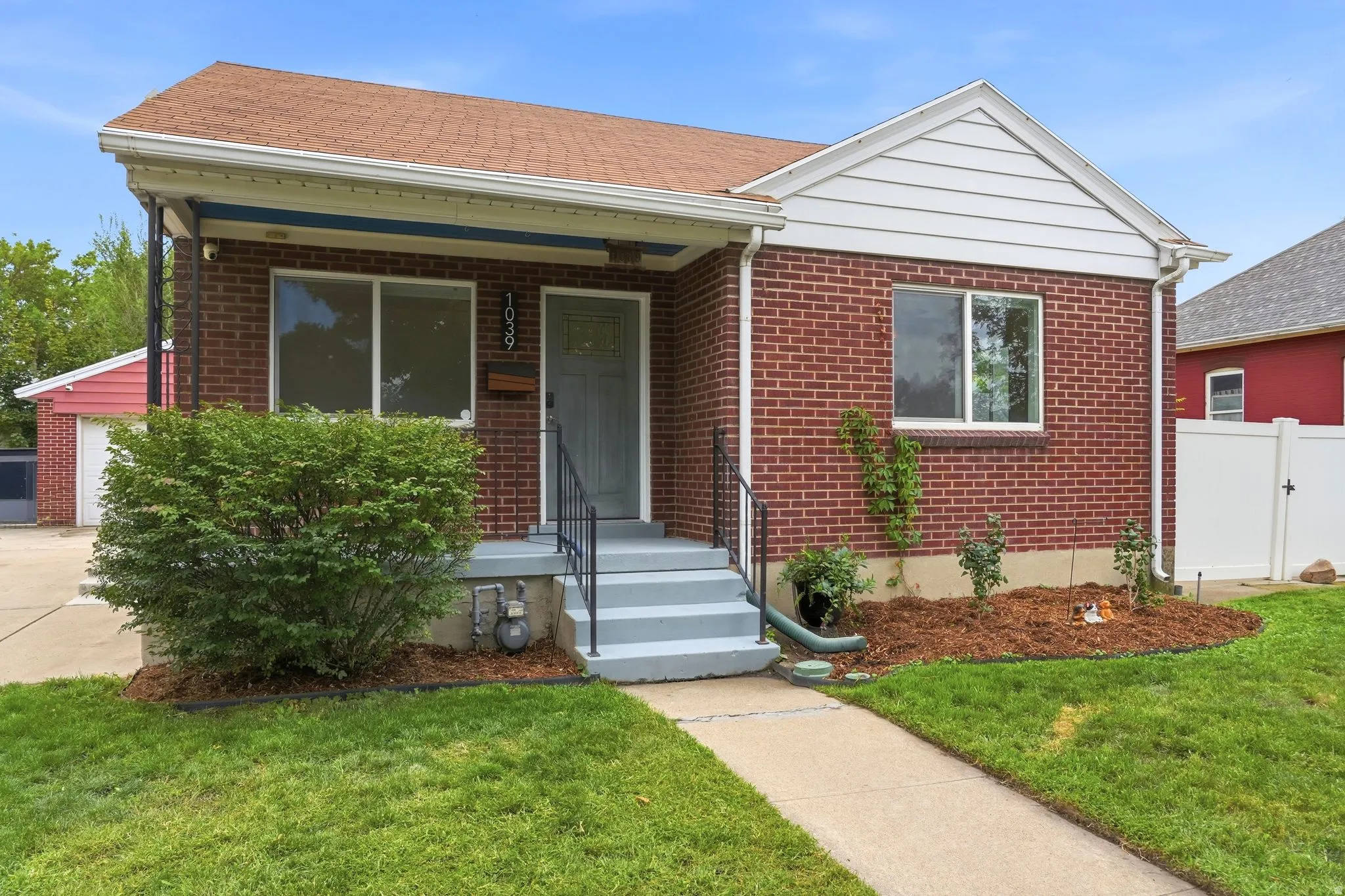 Brick exterior with white trim, covered front porch, concrete steps with metal railings, a manicured lawn, and a paved walkway