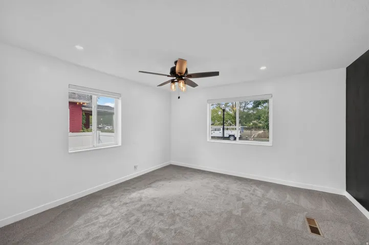 Spacious bedroom room with plush gray carpeting, recessed lighting, and a ceiling fan.