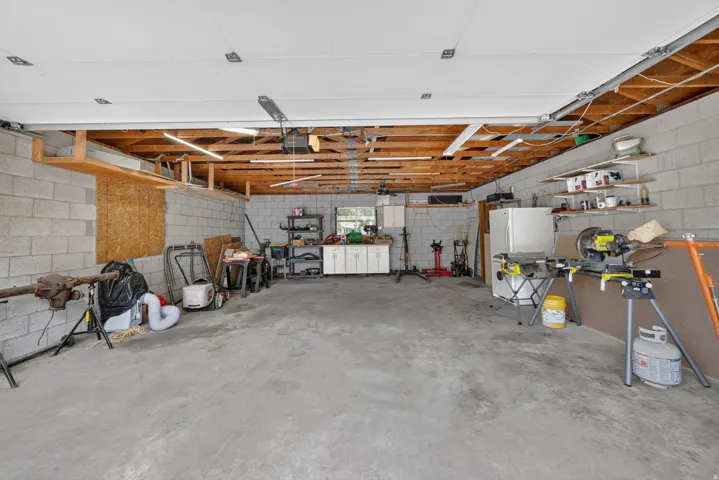 Spacious garage featuring concrete block walls, exposed wood beam ceiling, concrete flooring, and built-in shelving