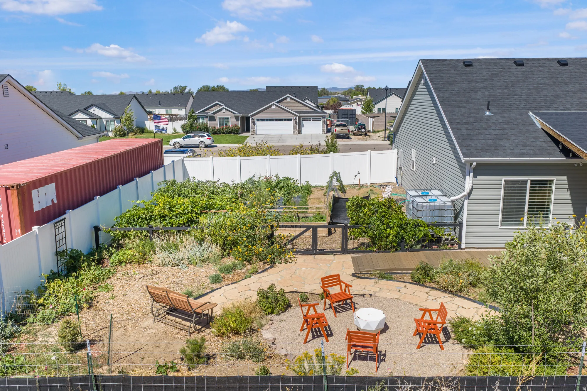 Gravel patio with a central fire pit, surrounded by garden beds, and a wood deck
