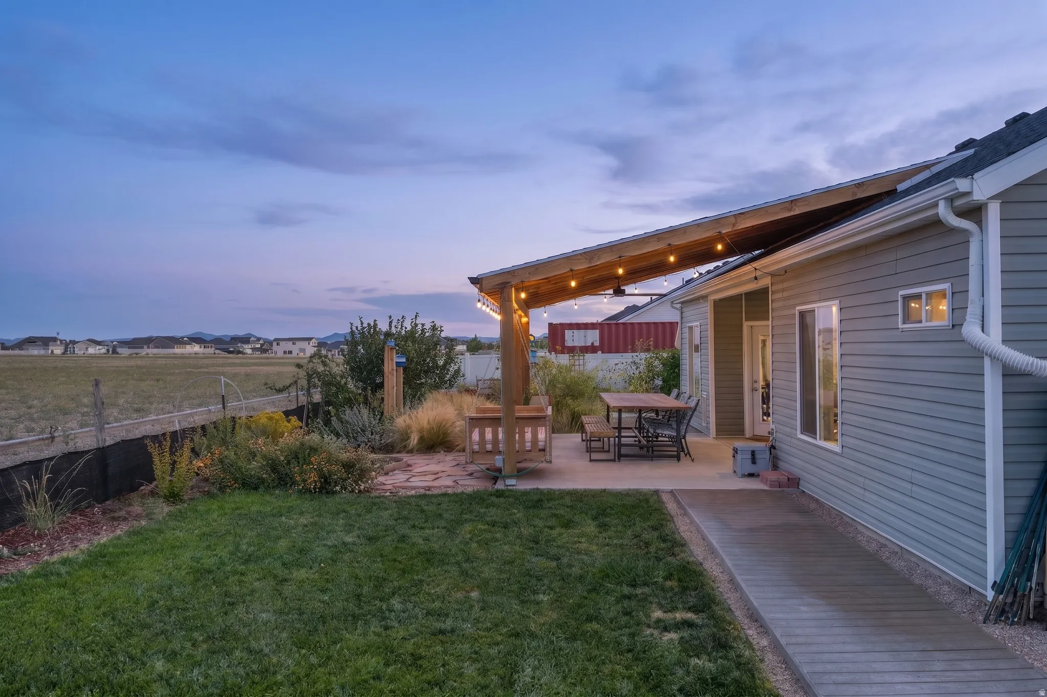 Expansive backyard featuring a concrete patio with a wood-framed overhead structure, gravel landscaping, and a manicured lawn