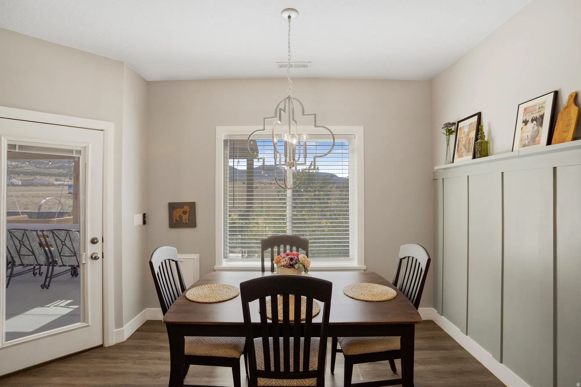 Wood-finish flooring throughout, board and batten wall detailing, large window with blinds, and an overhead chandelier with a geometric design