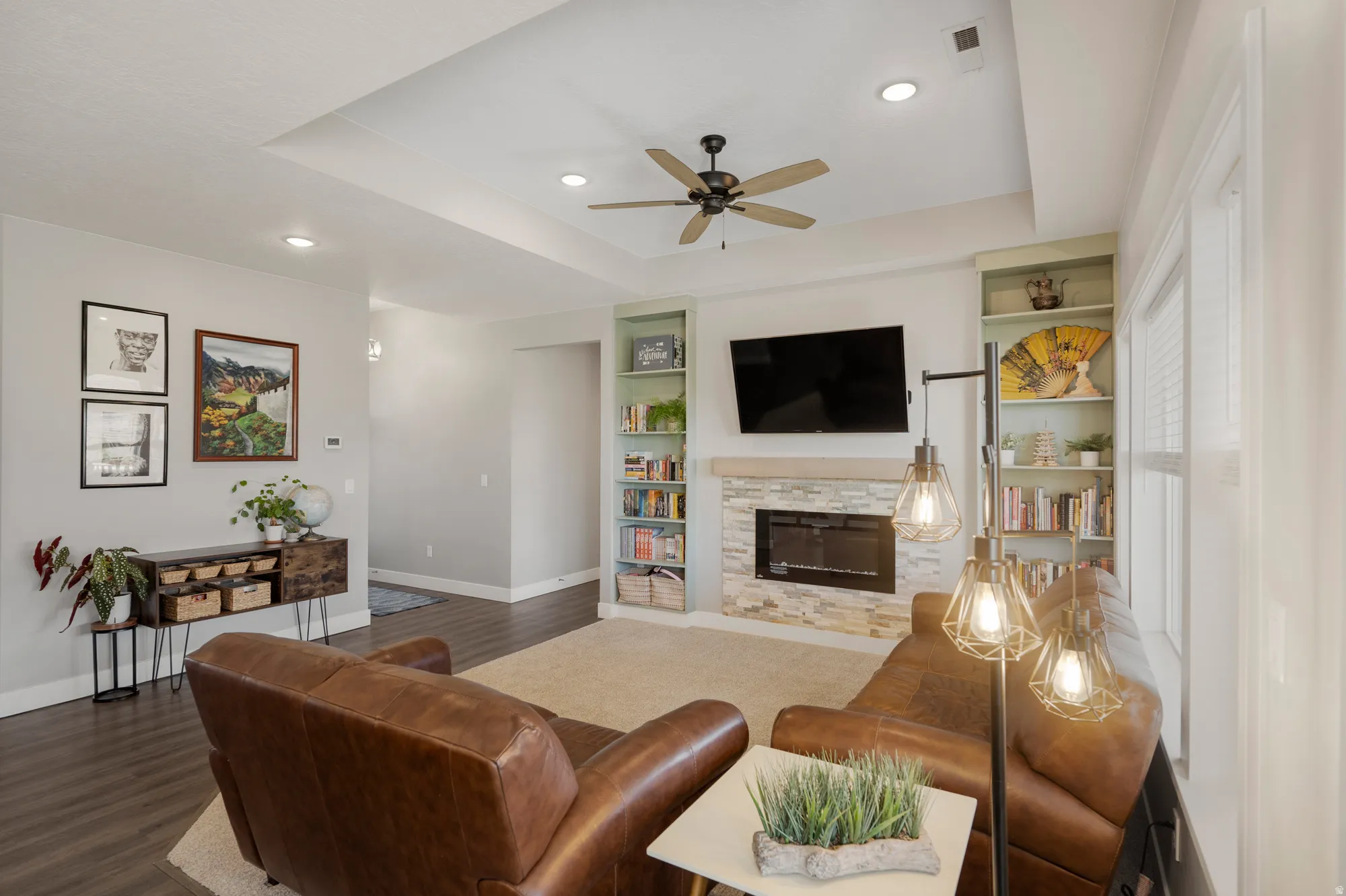Recessed lighting, tray ceiling, ceiling fan, stone-surround fireplace, and built-in shelving