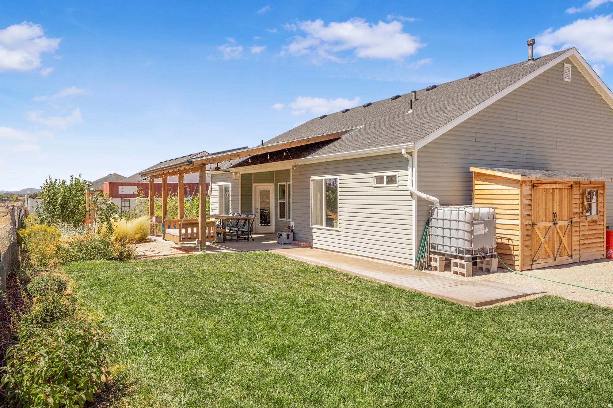 Expansive green lawn with a concrete patio, wood-framed pergola, and mature landscaping