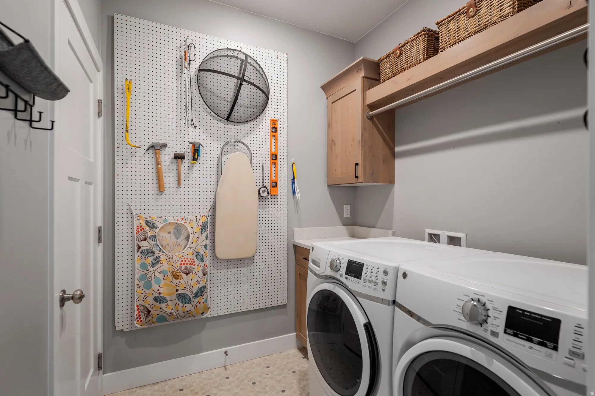 Laundry area featuring a pegboard wall, wood-finish cabinetry, a white countertop, and a built-in hanging rod