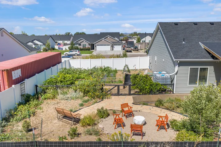 Gravel patio with a central fire pit, surrounded by garden beds, and a wood deck