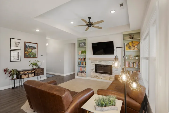 Recessed lighting, tray ceiling, ceiling fan, stone-surround fireplace, and built-in shelving