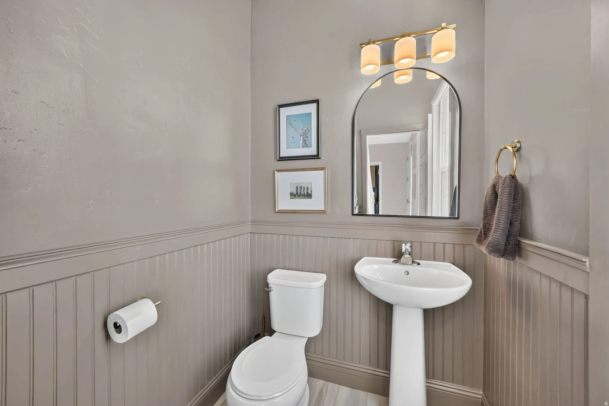 Pedestal sink with chrome faucet, arched mirror, and three-light vanity fixture