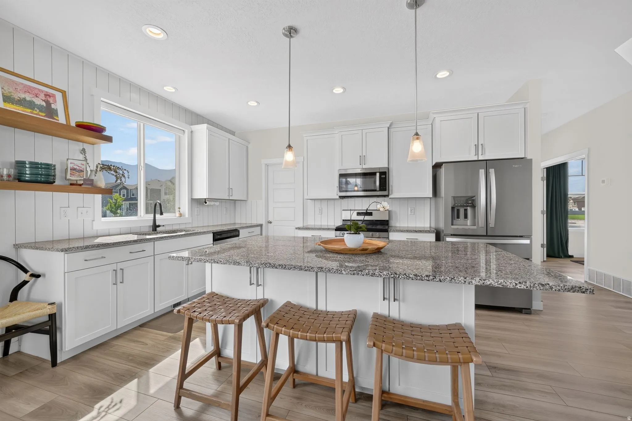 Kitchen featuring white cabinetry, wood-finish flooring, a central island with granite countertop, stainless steel appliances, and pendant lighting