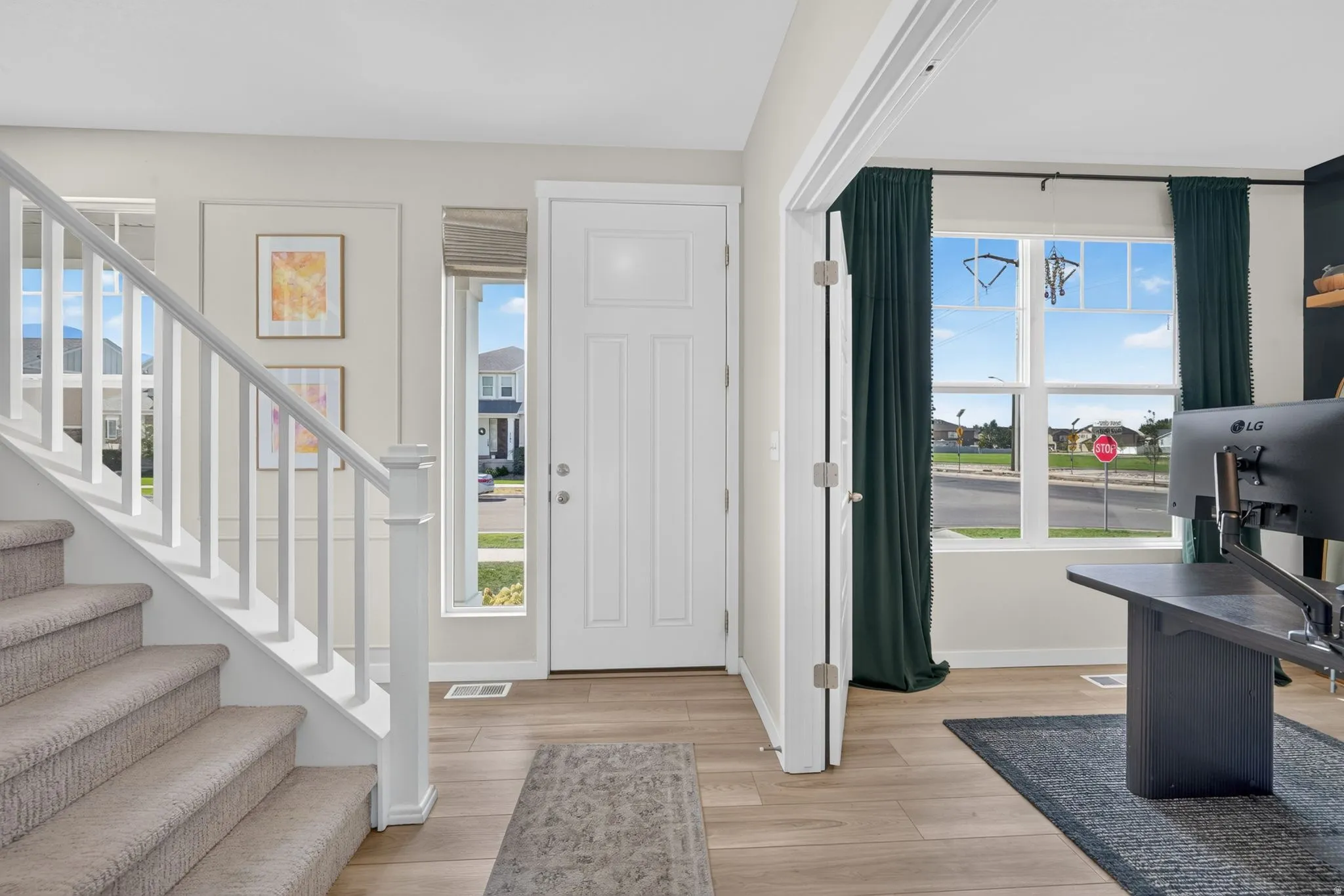 Wood-finish flooring throughout, white paneled entry door, and a staircase with carpeted treads