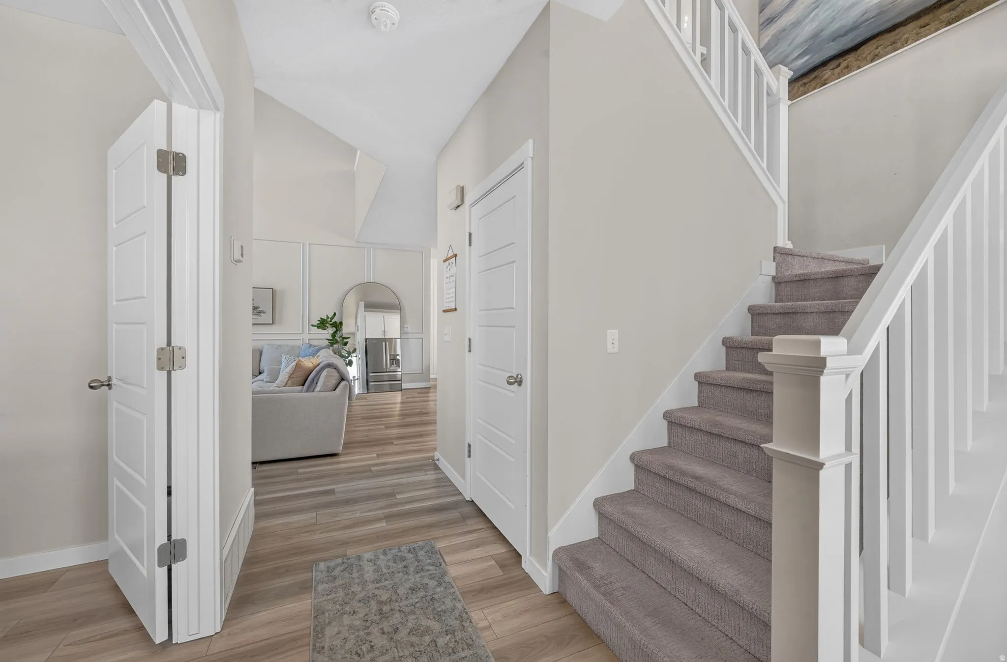 Vaulted ceiling, wood-finish flooring, paneled interior doors, and a carpeted staircase with white balusters