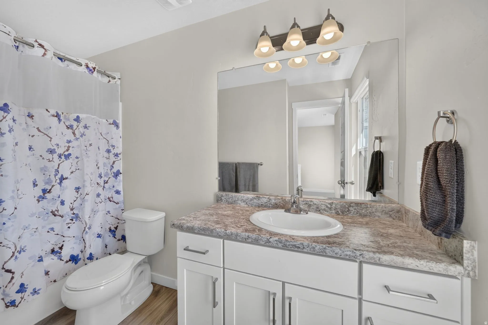 Bathroom featuring a white vanity with slab-panel doors, brushed nickel hardware, an integrated sink, and a speckled countertop