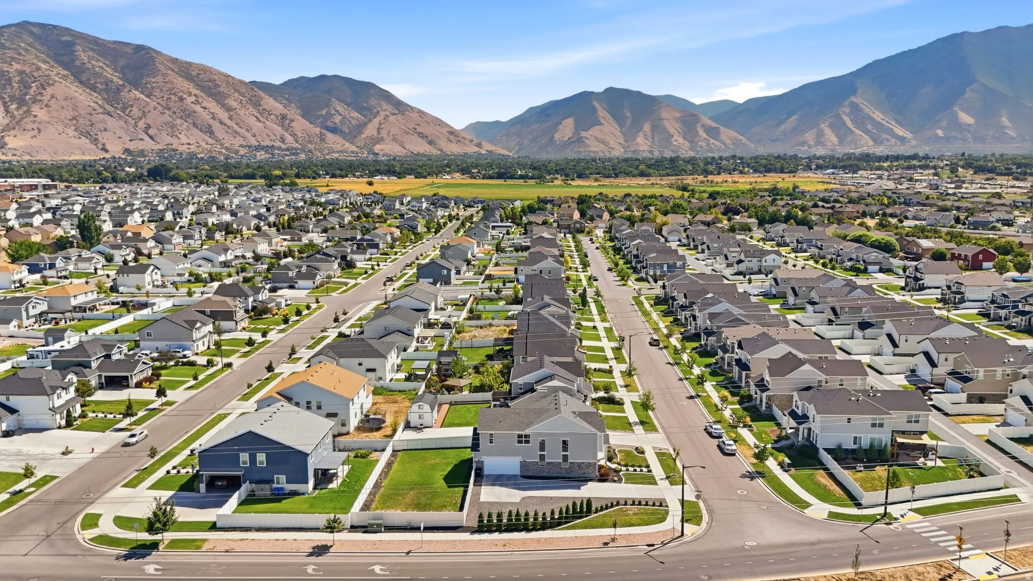 Expansive neighborhood setting with paved streets and sidewalks, surrounded by mountain scenery and open green spaces