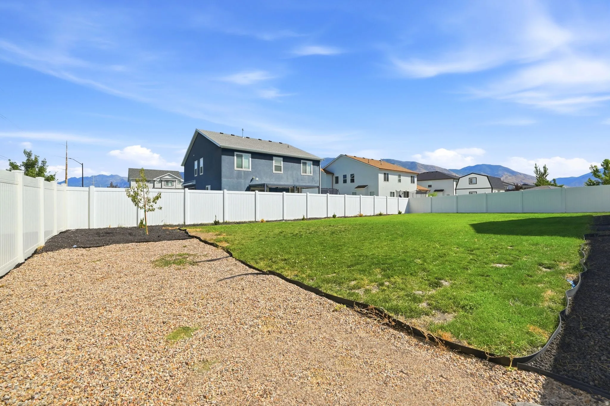 Expansive backyard featuring a large green lawn, gravel patio area, and white privacy fencing