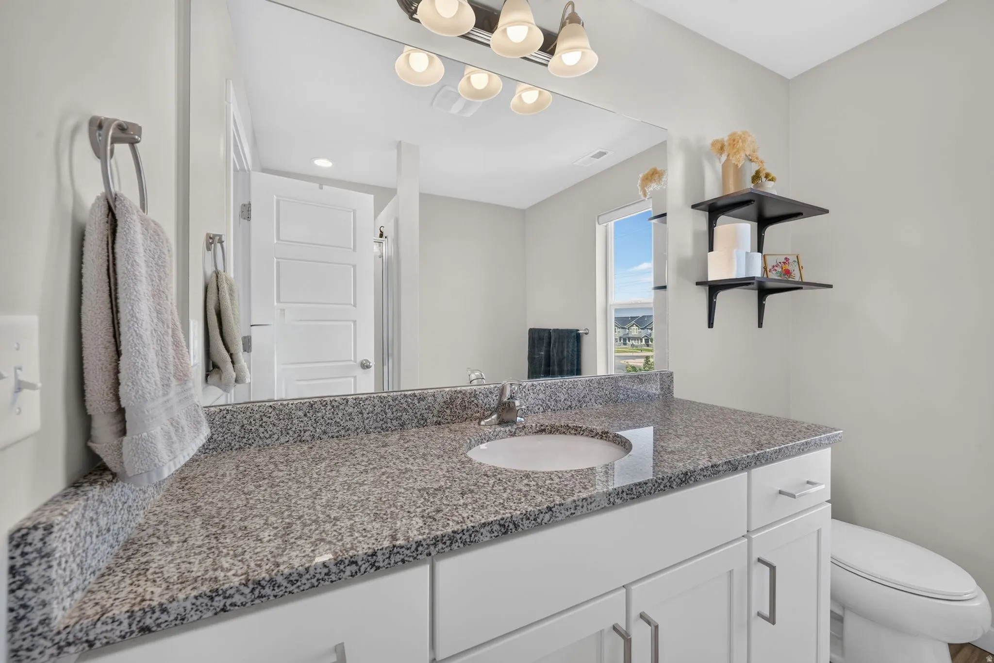 Spa-inspired bathroom featuring a spacious speckled stone countertop with dual sink basins, white cabinetry with hardware accents, and a modern pendant light fixture