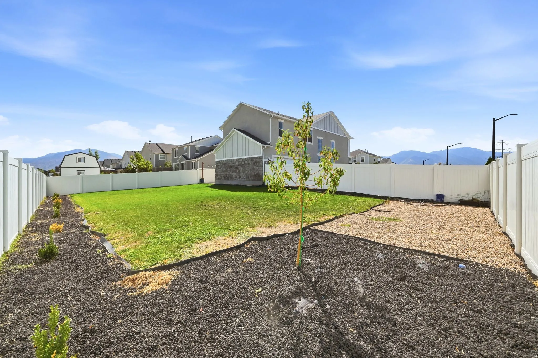 Fenced backyard featuring a manicured lawn, dedicated planting areas, and a gravel-finish section