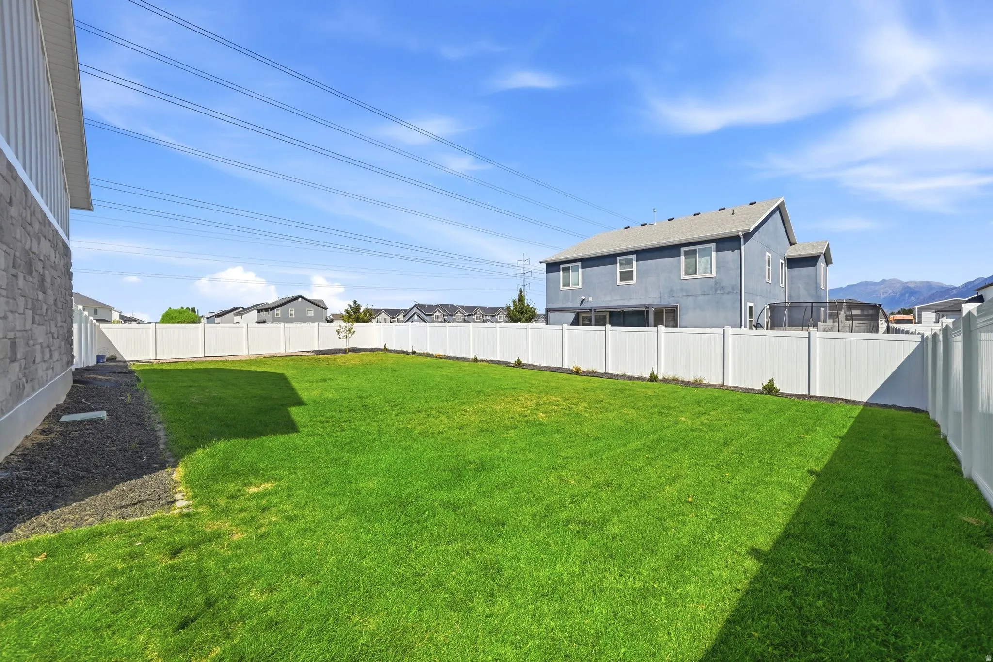 Expansive backyard featuring a manicured lawn, full privacy fencing, and stone veneer and siding exterior