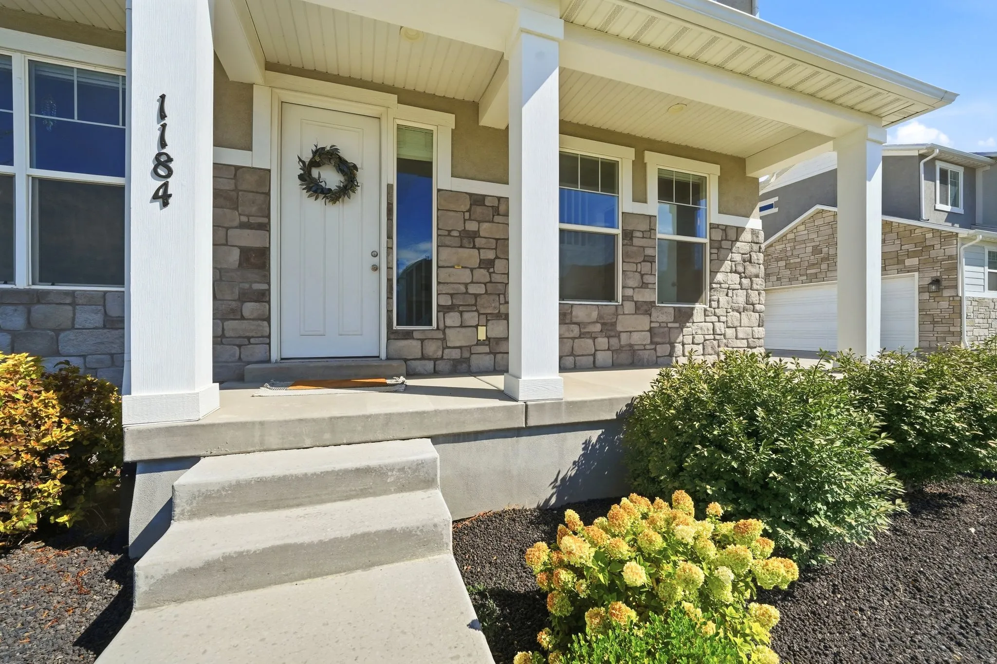 Covered porch with stone and stucco exterior, white paneled entry door, and concrete steps
