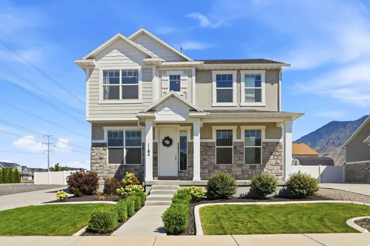 Two-story residence featuring a stone and siding facade, covered front porch, and manicured front landscaping