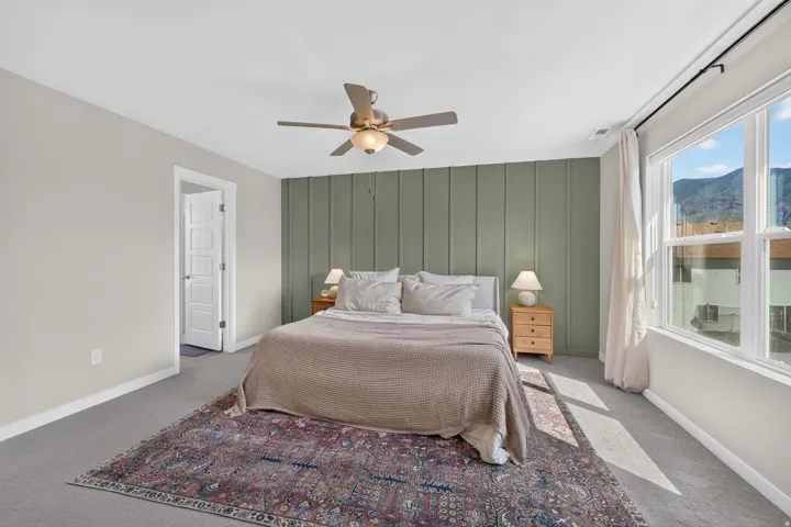 Recessed panel accent wall, ceiling fan with integrated lighting, large windows, mountain backdrop, and light-colored carpeting