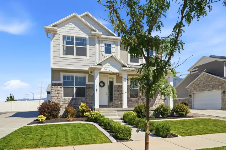 Two-story facade with stone and siding accents, prominent gabled roofline, front-facing attached garage, concrete driveway, and a landscaped front yard with a walkway