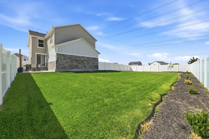 Expansive rear yard featuring a manicured lawn, a white privacy fence, and a stone and stucco exterior with a sliding glass door leading to an outdoor patio