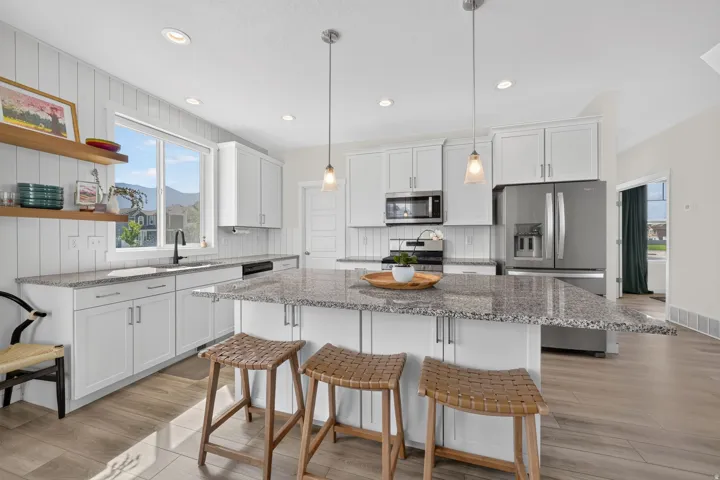 Kitchen featuring white cabinetry, wood-finish flooring, a central island with granite countertop, stainless steel appliances, and pendant lighting